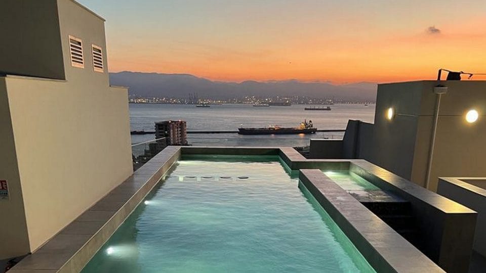 Gibraltar Upper Town Property Rooftop infinity pool in Gibraltar’s Upper Town overlooking the Bay of Gibraltar at sunset, with sea views, anchored ships, and modern apartment terraces.