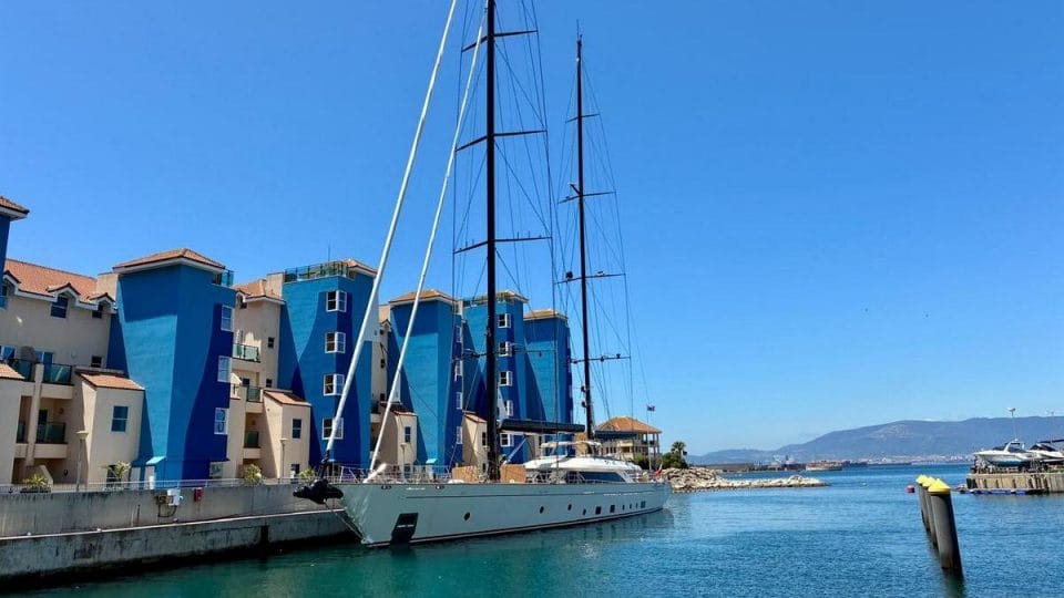 Luxury yacht moored in Gibraltar marina with waterfront apartments and Mediterranean views on a sunny day.